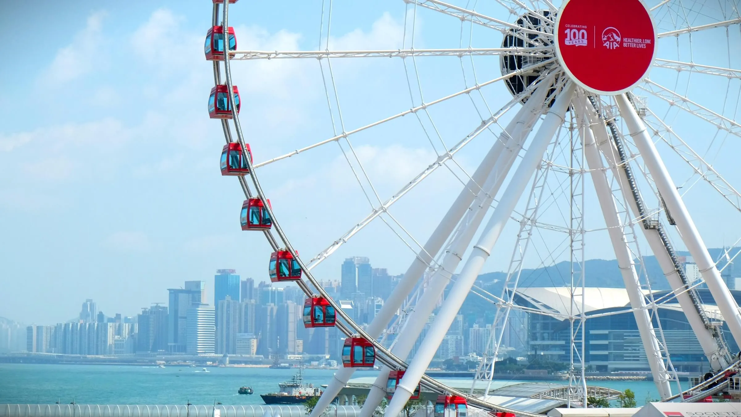 Red gondolas on the Hong Kong Observation Wheel on a sunny day, with Victoria Harbour, the Convention and Exhibition Centre and the towers of Wan Chai behind