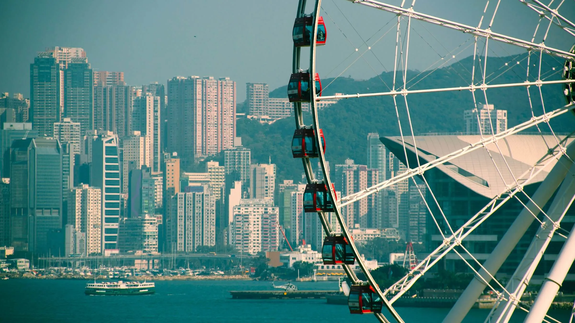 Red gondolas on the rim of the Hong Kong Observation Wheel, with a Star Ferry crossing Victoria Harbour and Wan Chai behind
